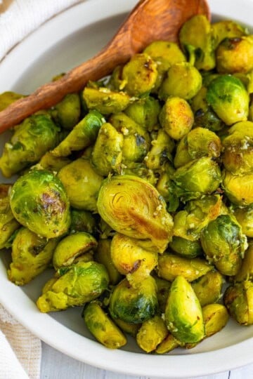 A plate of golden sauteed brussel sprouts tossed in garlic butter with a wooden spoon.