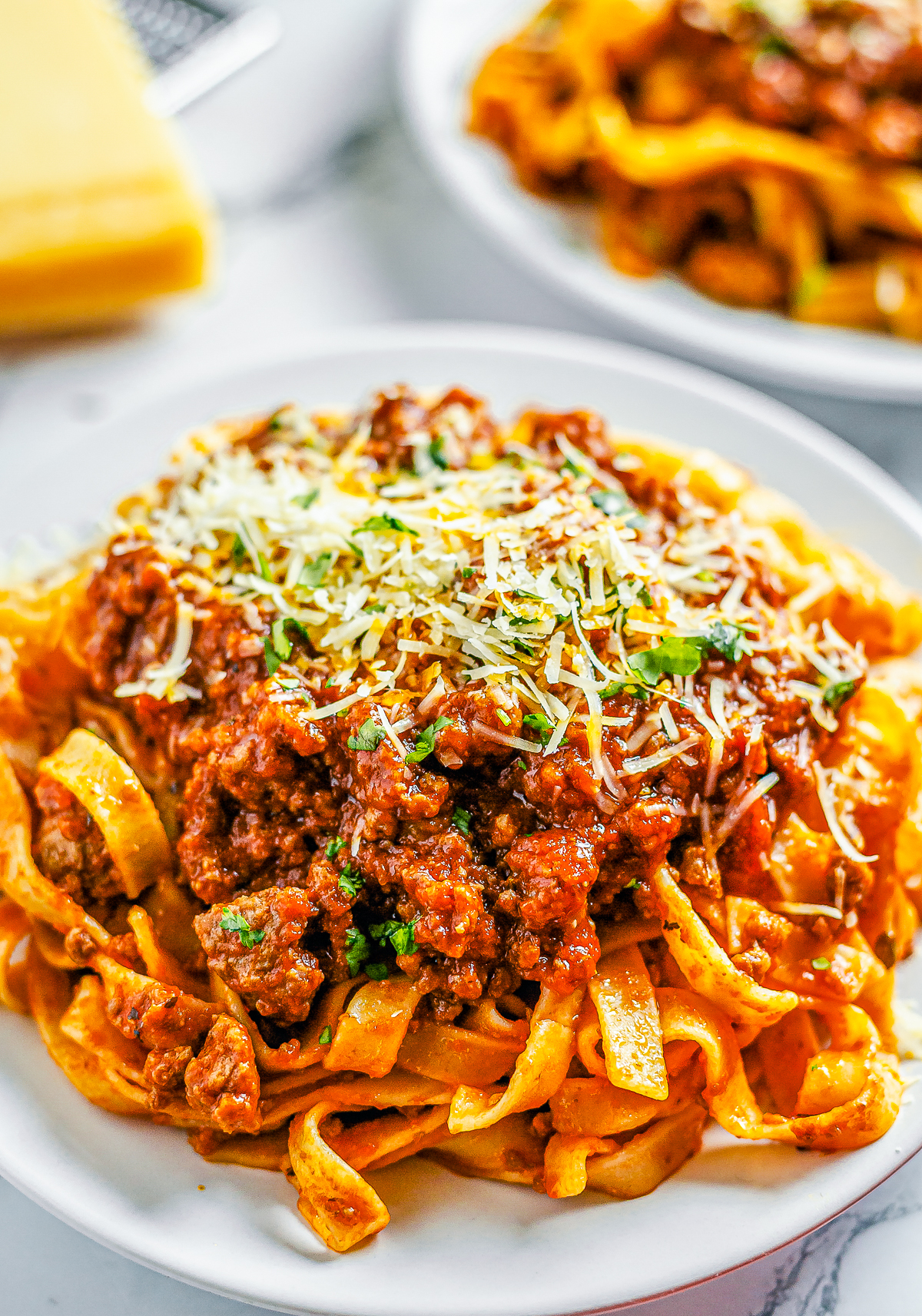 Close up of Meat Sauce Recipe over pasta on plate topped with cheese and parsley.