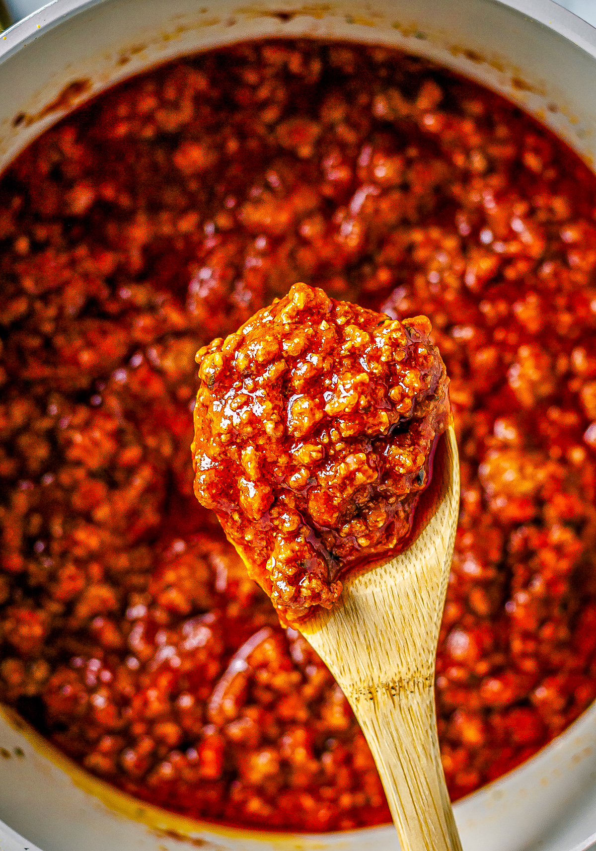 Wooden spoon holding up some of the Meat sauce Recipe from pan.