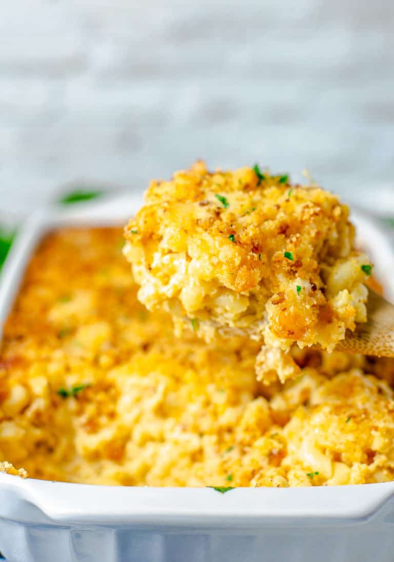 A wooden spoon scooping creamy Baked Mac and Cheese with cornbread crust out of a white baking dish.