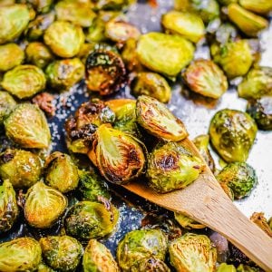 Square image of finished Brussel Sprouts on baking pan with some on wooden spoon.
