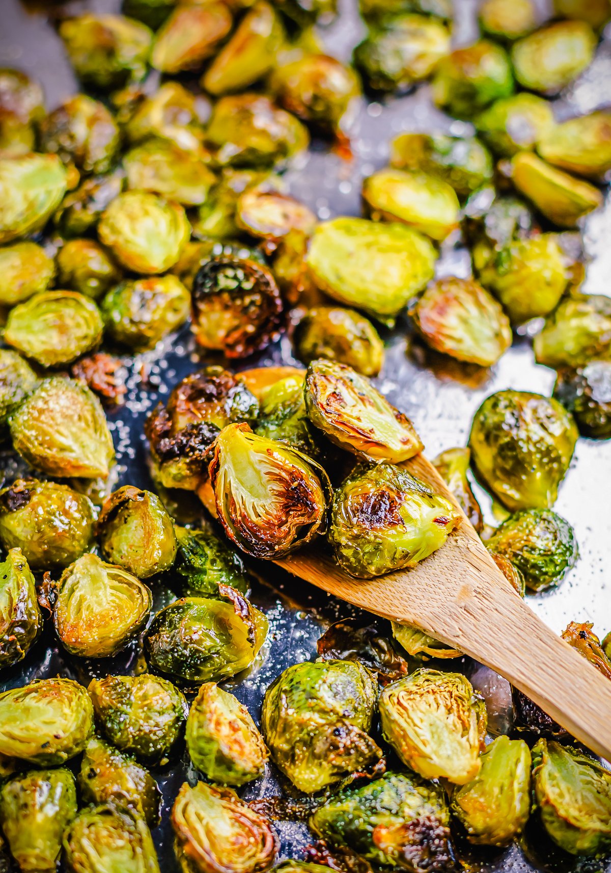 Oven Roasted Brussel Sprouts on baking sheet with some on wooden spoon,