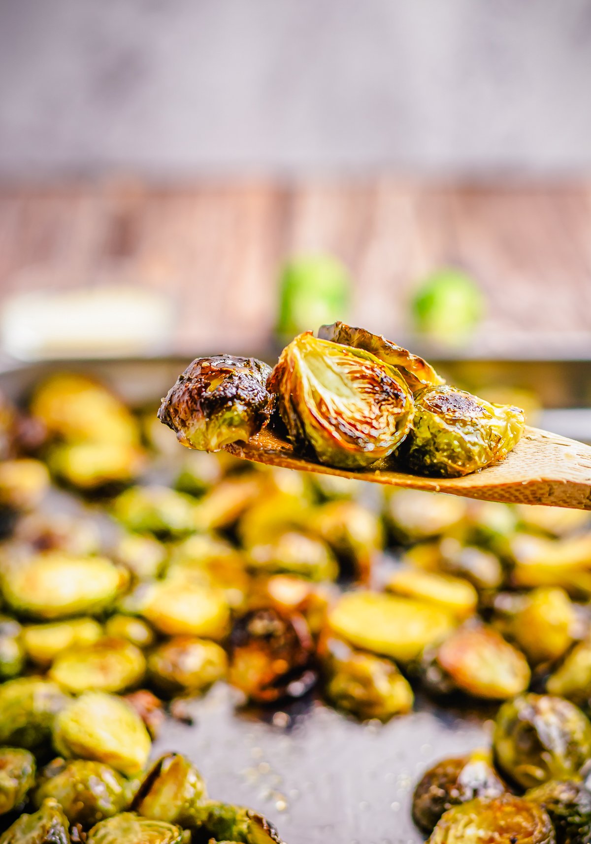 Wooden spoon lifting up finished Oven Roasted Brussel Sprouts off baking sheet.