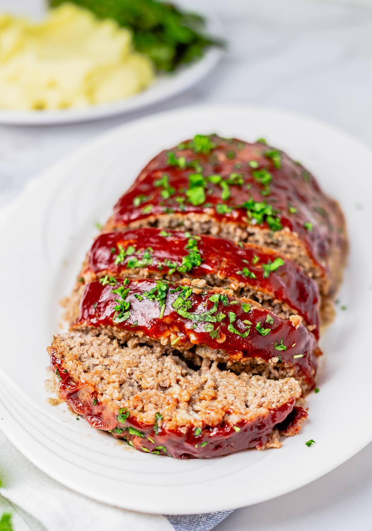 Finished Easy Meatloaf on white platter sliced and topped with parsley.