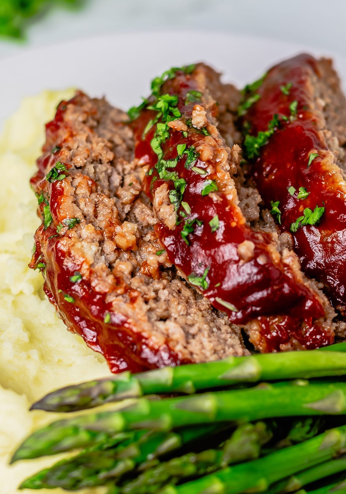 Close up of sliced Easy Meatloaf with mashed potatoes and asparagus.