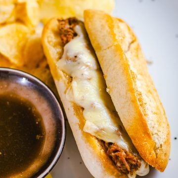 A crock pot french dip sandwich with melted provolone served with au jus and chips