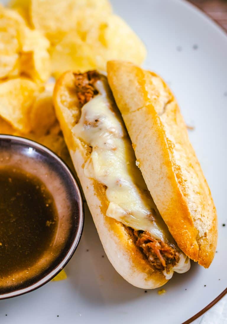 A crock pot french dip sandwich with melted provolone served with au jus and chips