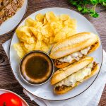 Square photo of Crock Pot French Dip Sandwiches on plate with chips.