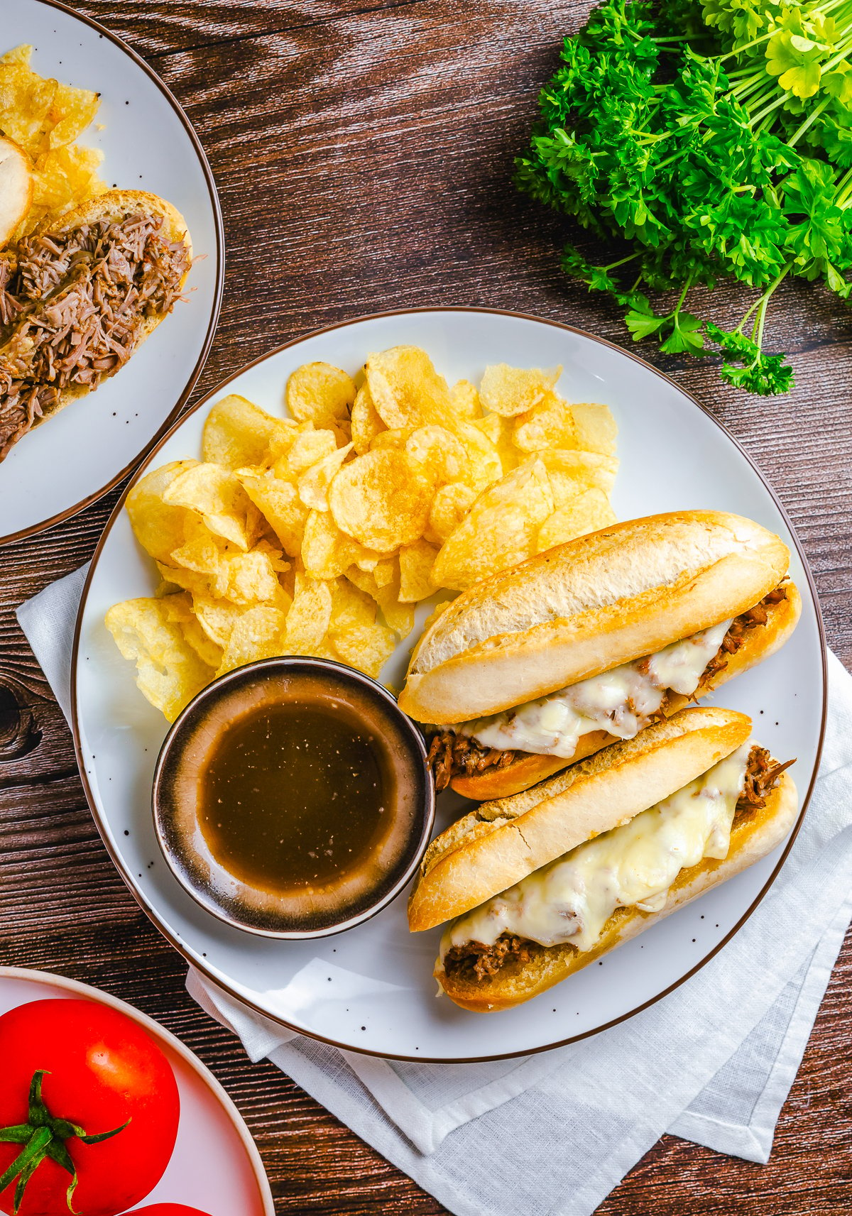 Overhead with French Dip Sandwiches on white plate with au jus and chips.