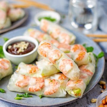 A plate of fresh spring rolls filled with shrimp, lettuce, and noodles served with hoisin peanut dipping sauce.