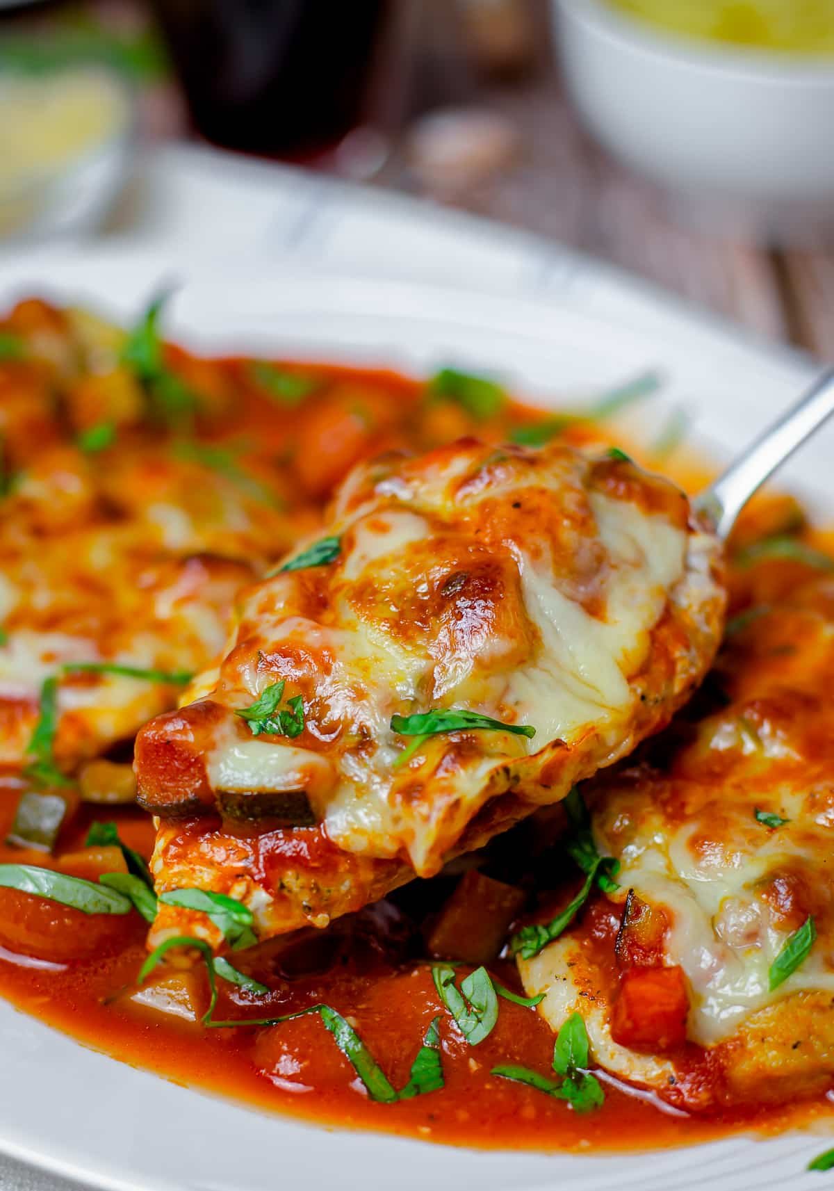 Straight on image of Healthy Chicken Parmesan with serving spoon holding up a piece of chicken. White platter.