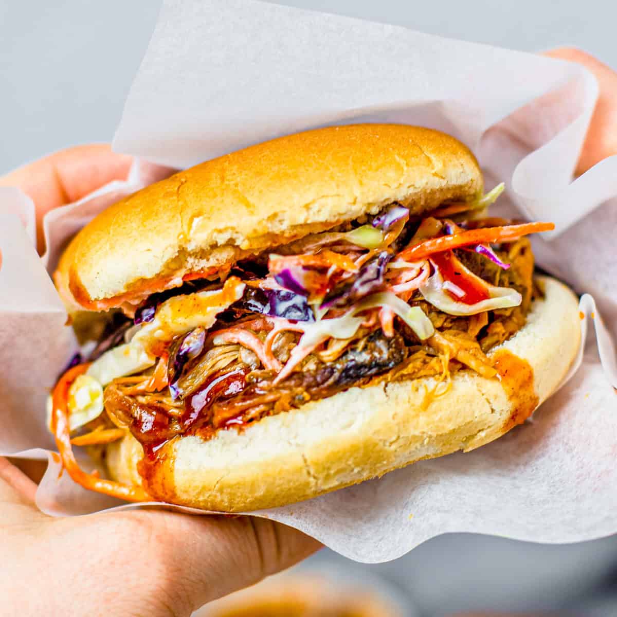 A hand holding a crockpot pulled pork sandwich with BBQ sauce and coleslaw.