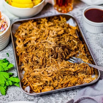 A tray of tender crock pot pulled pork served with cookout sides.