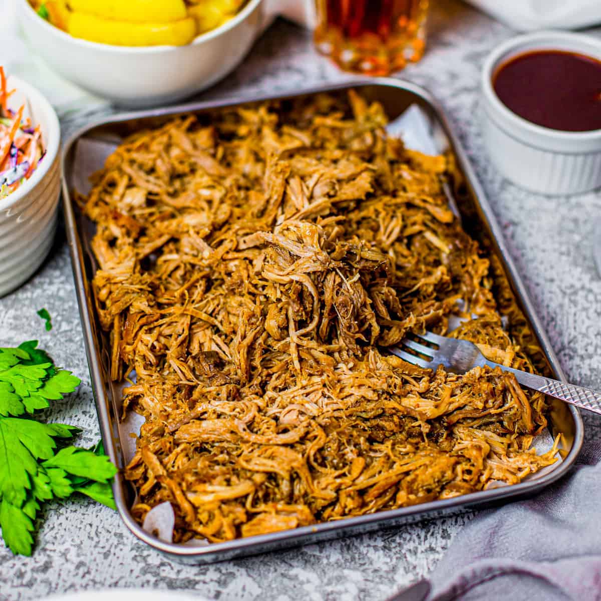 A tray of tender crock pot pulled pork served with cookout sides.