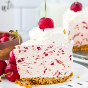 Square image of slice of cheesecake on white plate showing cherries in the mixture