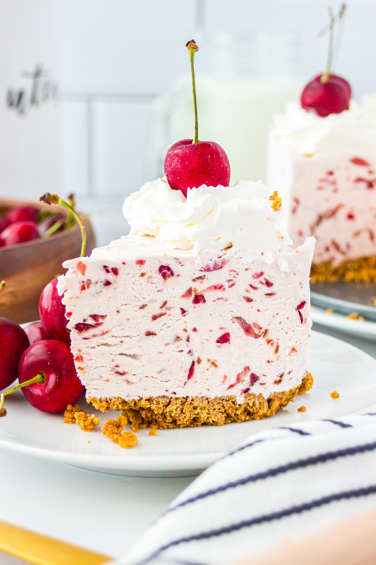 Slice of No Bake Cherry Cheesecake on white plate topped with whipped cream and a cherry