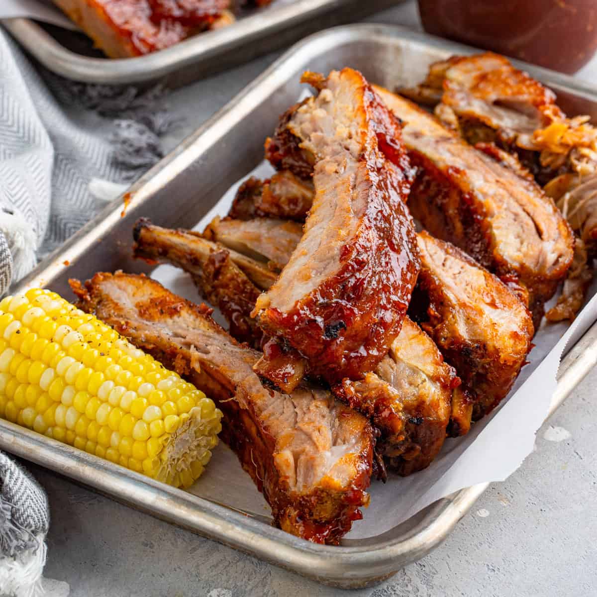 A tray of glazed BBQ baby back ribs served with corn on the cob.