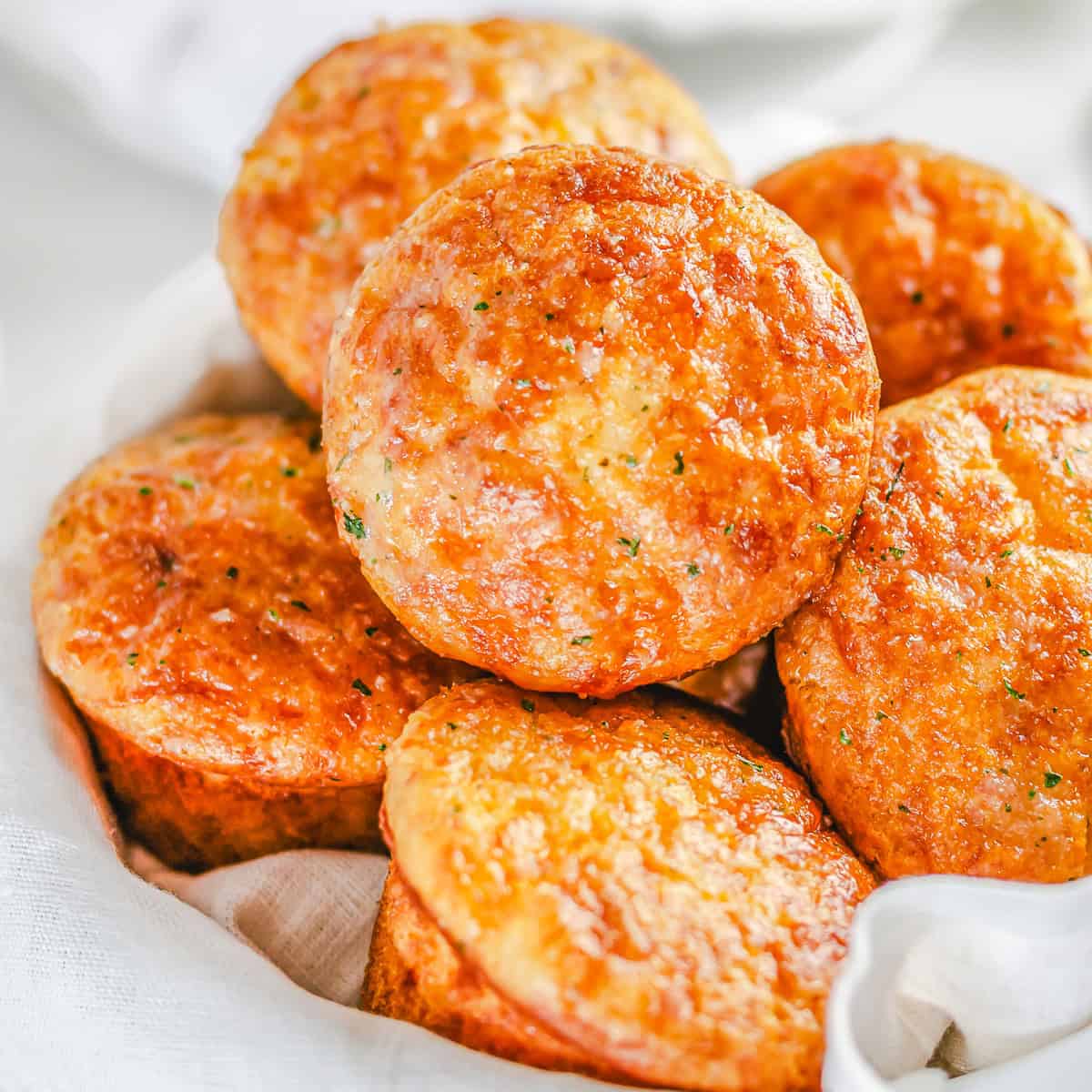 Golden garlic cheddar cheese muffins stacked in a basket lined with a white towel.