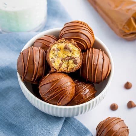 A bowl of chocolate covered cookie dough truffles with one cut open to show the center.