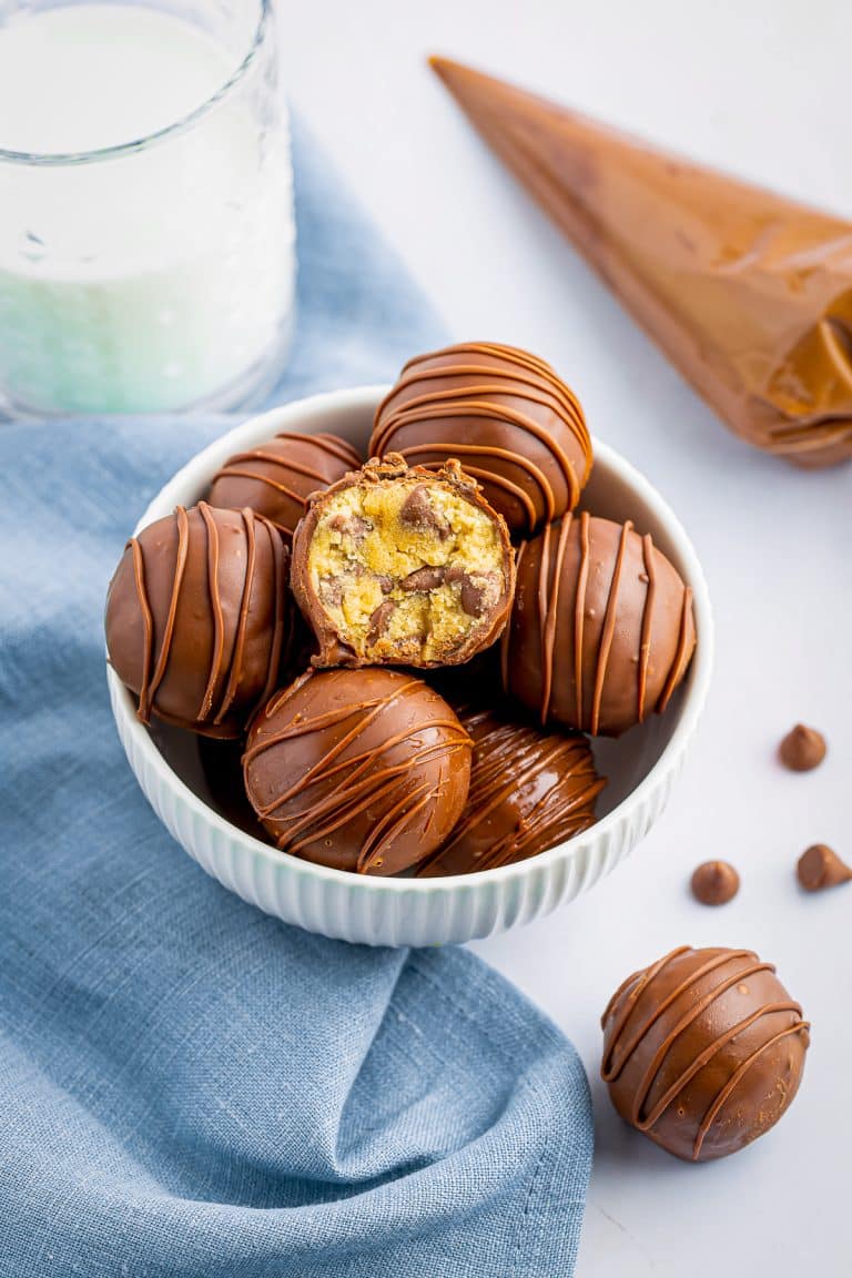 A bowl of chocolate covered cookie dough truffles with one cut open to show the center.