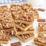 A stack of toffee bars with chocolate and pecan topping next to milk and pieces of milk chocolate.