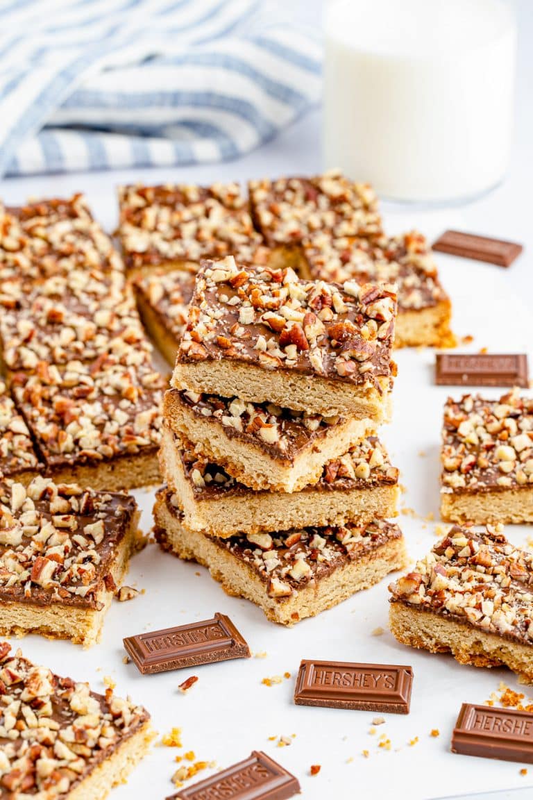 A stack of toffee bars with chocolate and pecan topping next to milk and pieces of milk chocolate.