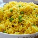 A bowl of homemade yellow rice with peas, golden from turmeric and flecked with green peas.