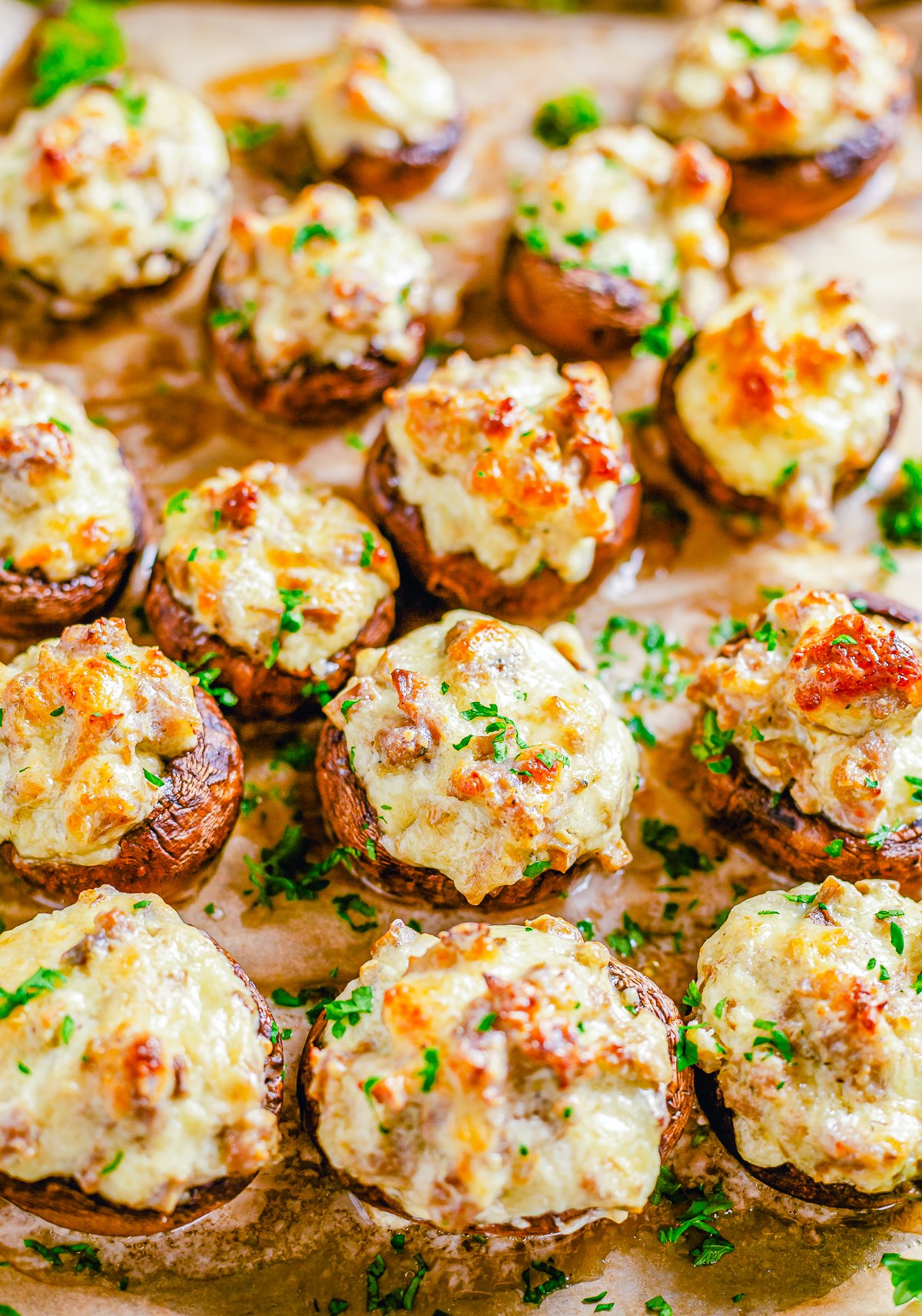 Overhead close up of finished Sausage Stuffed Mushrooms on wooden board.