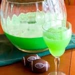 A punch bowl and glass of bright green football punch with chocolate footballs on the table.