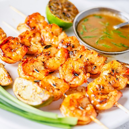 Square image of grilled shrimp on white plate with sauce