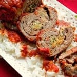 Sliced beef braciole on a white platter topped with tomato sauce and fresh basil.