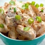 Close up of creamy red potato salad topped with sliced green onions in a teal bowl