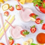 Overhead of two smoothies surrounded by strawberries and bananas