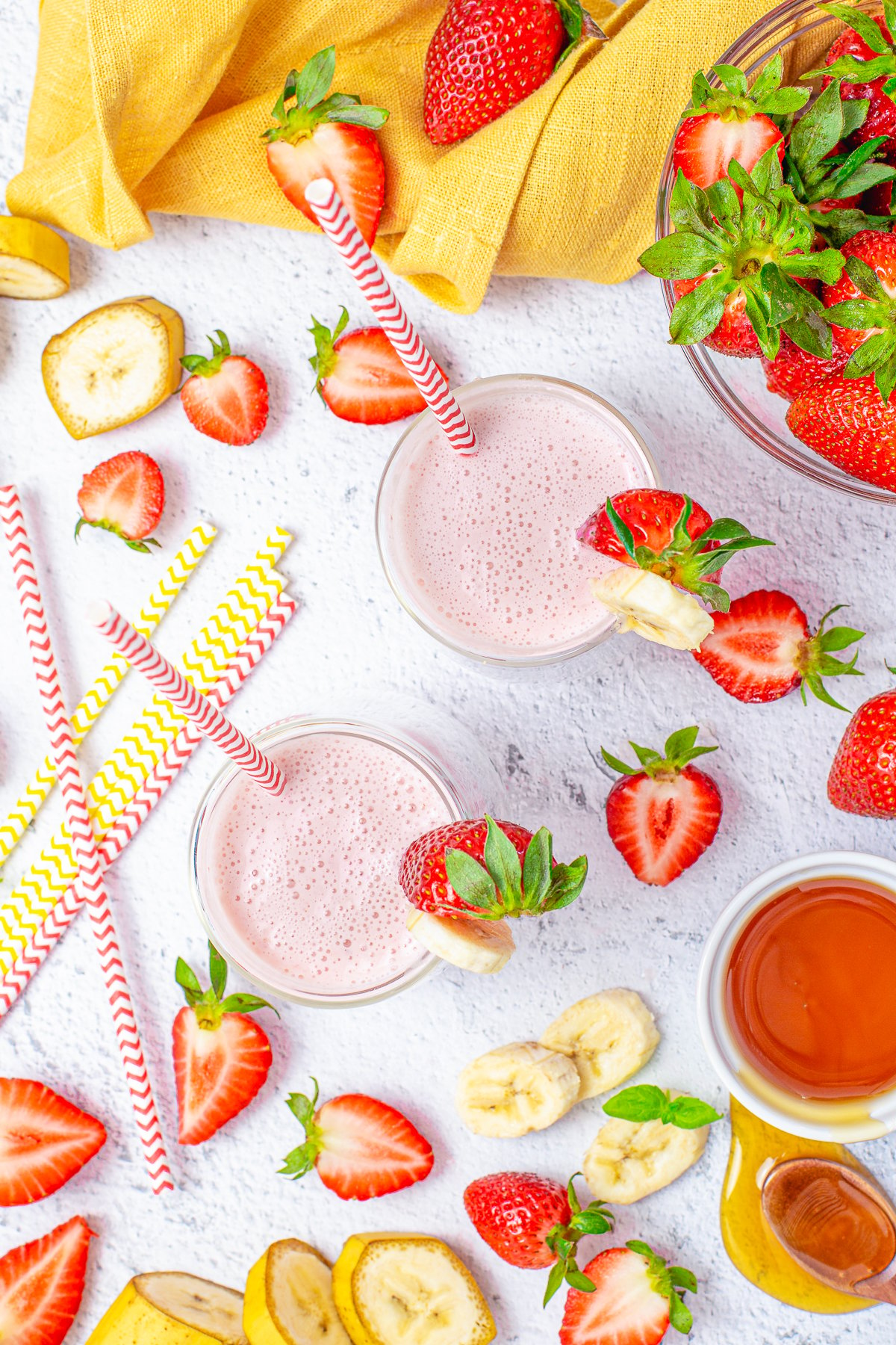 Overhead of two smoothies surrounded by strawberries and bananas