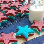 Stacked red and blue velvet Patriotic Brownie Sandwich Cookies with a glass of milk on a red gingham cloth.