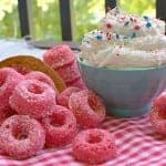 Pink sugared Baked Donuts piled beside a bowl of fluffy funfetti dip with sprinkles.