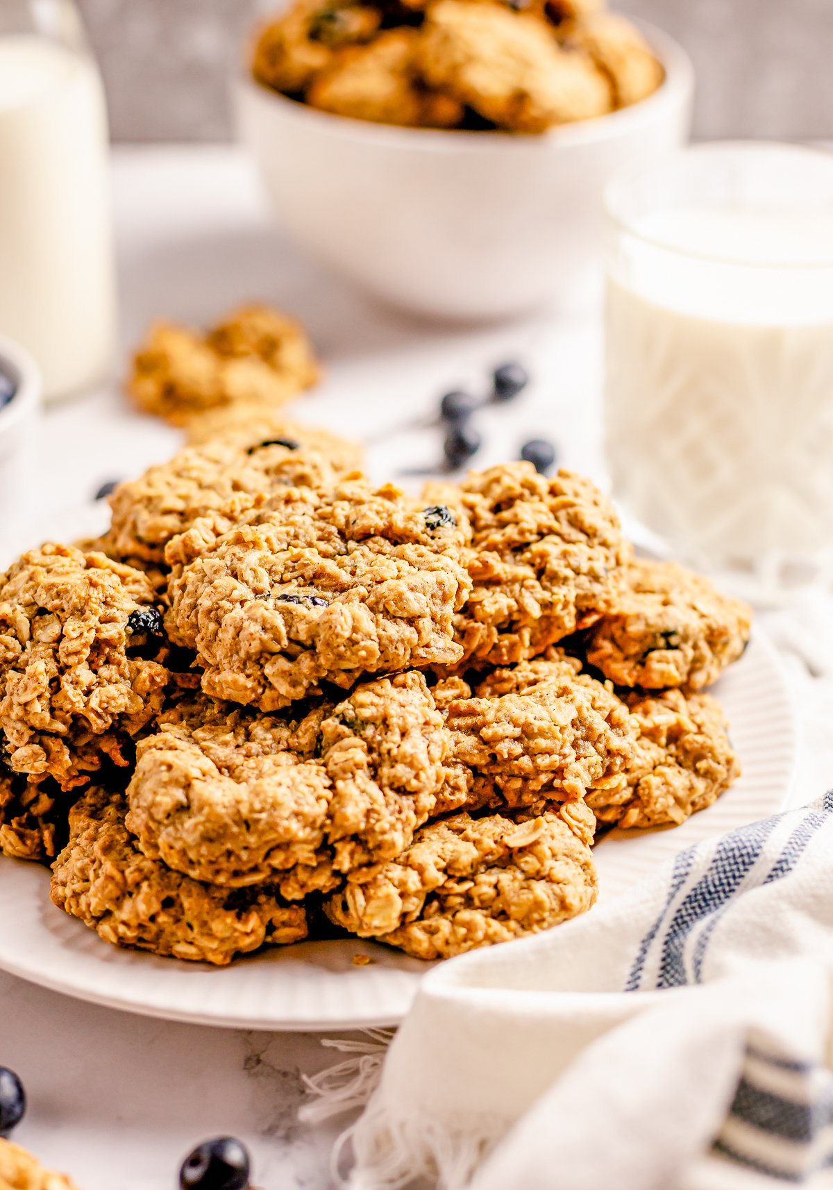 Stacked Oatmeal Blueberry Cookies on plate with milk in background.