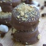 A stack of homemade oreo ice cream sandwiches coated in milk chocolate and graham cracker crumbs with mini marshmallows scattered around.