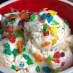 Scoops of cereal milk ice cream in a red bowl topped with fruity pebbles cereal