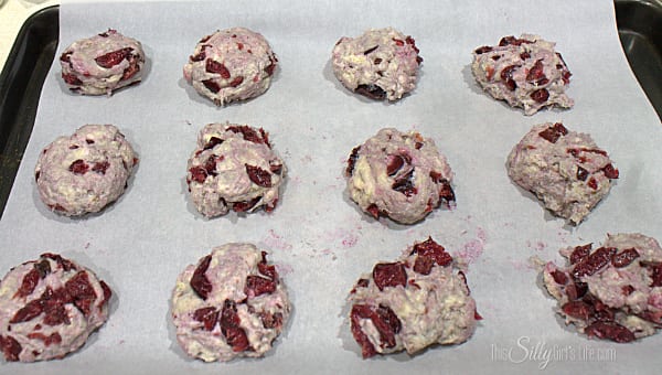 Mix in the cherries, try not to get as much of the excess cherry juice in as you can. Mix with your hands until combined. On a sheet tray lined with parchment paper or a silicone baking mat, roll in your hands 2 inch balls of dough. Place on the cookie sheet, flatten dough balls to 1 inch thick. 