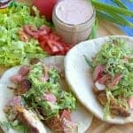 Two chicken pitas loaded with marinated chicken, dressed lettuce, and tomatoes on a wooden board.