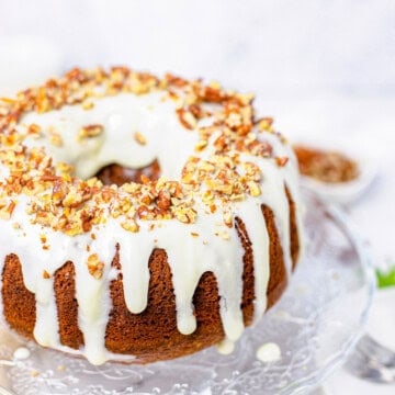 A whole hummingbird bundt cake drizzled with cream cheese glaze and topped with toasted pecans