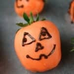 A halloween chocolate covered strawberry decorated like a jack-o-lantern pumpkin with a chocolate face.