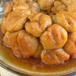 A golden pull apart apple cinnamon monkey bread on a white plate drizzled with caramel glaze.