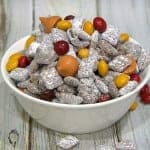 Halloween muddy buddies in a white bowl with candy coated chocolates and pumpkin spice kisses.