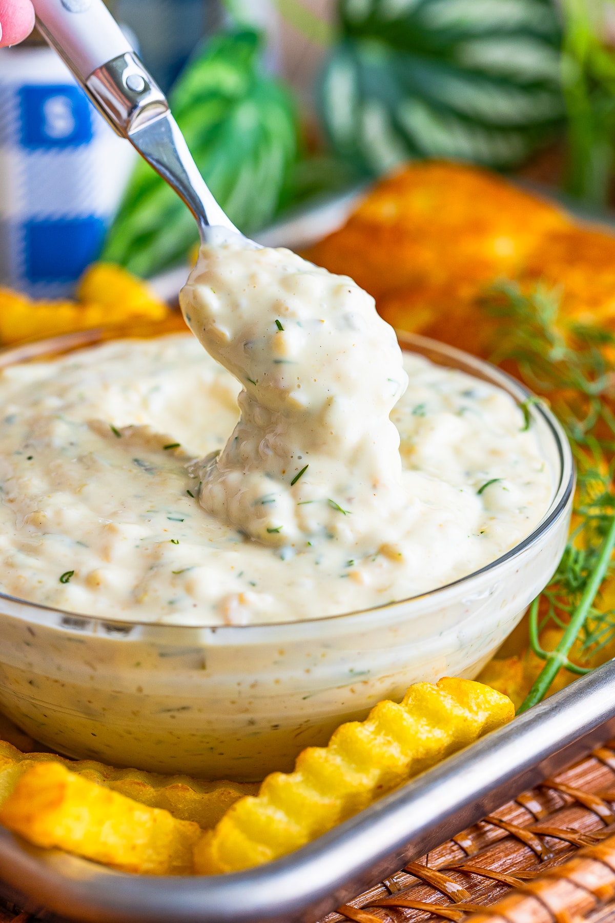a spoon with easy tartar sauce dripping off of it into a clear bowl