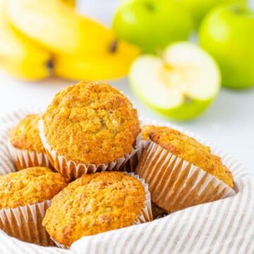 Apple Banana Oat Muffins in basket with apples and bananas in background.