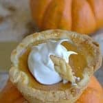 A Mini Pumpkin Pie topped with whipped cream and a pastry leaf sitting on a small pumpkin.