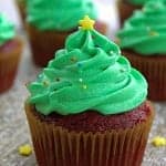 A Christmas tree cupcake with swirled green frosting, sprinkle ornaments, and a yellow star on top.