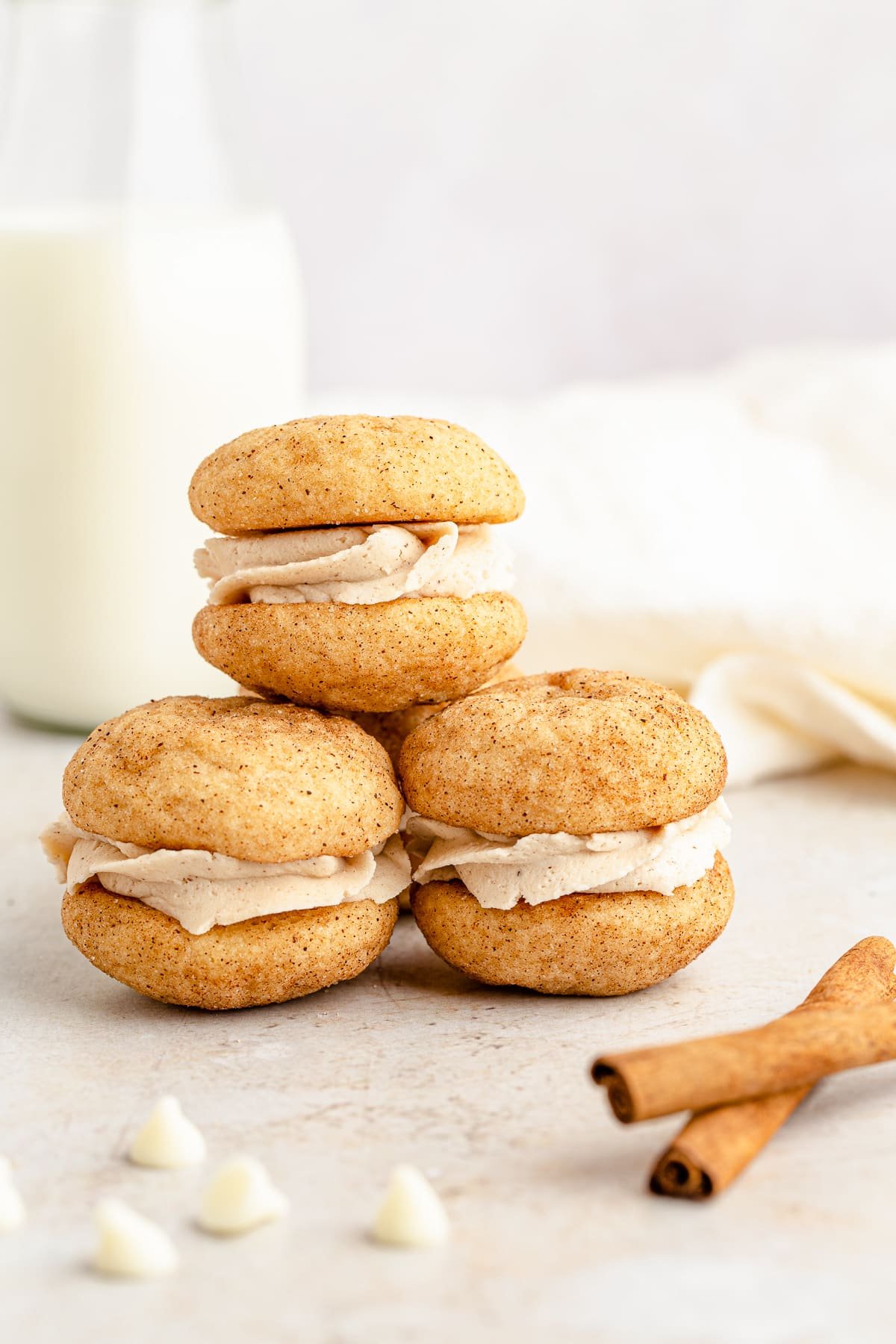 Three stacked Snickerdoodle Sandwich Cookies with cinnamon sticks and milk.